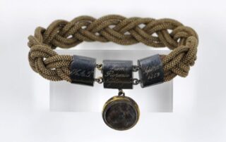 A woven bracelet, with a metal clasp and pendent that contains an lock of hair.