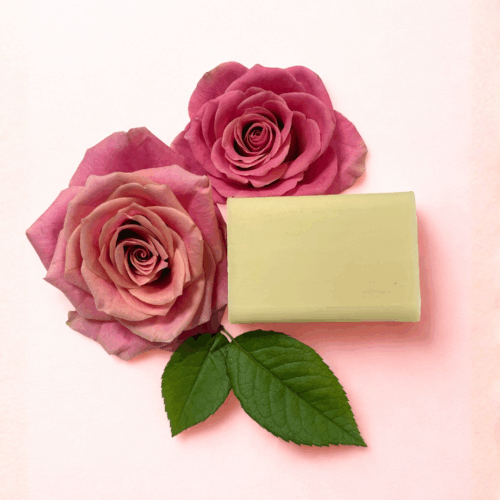 a bar of cream coloured soup surrounded by roses on a pale pink background