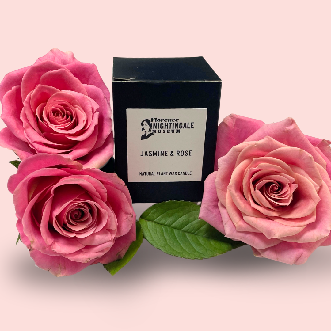 a boxed candle surrounded by pink roses