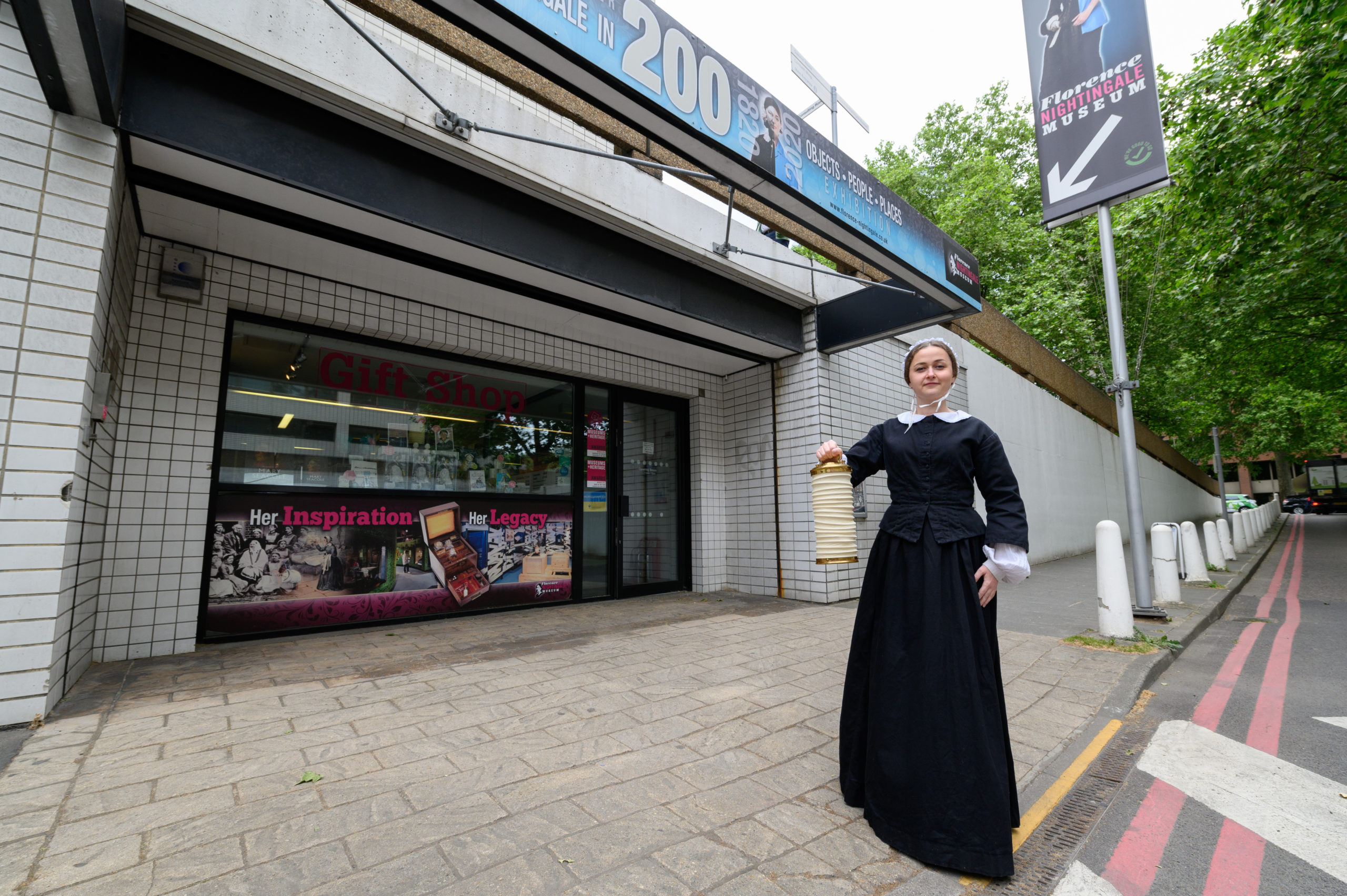 Florence Nightingale performer posing beside the Museum entrance. She holds a lamp out towards the camera.