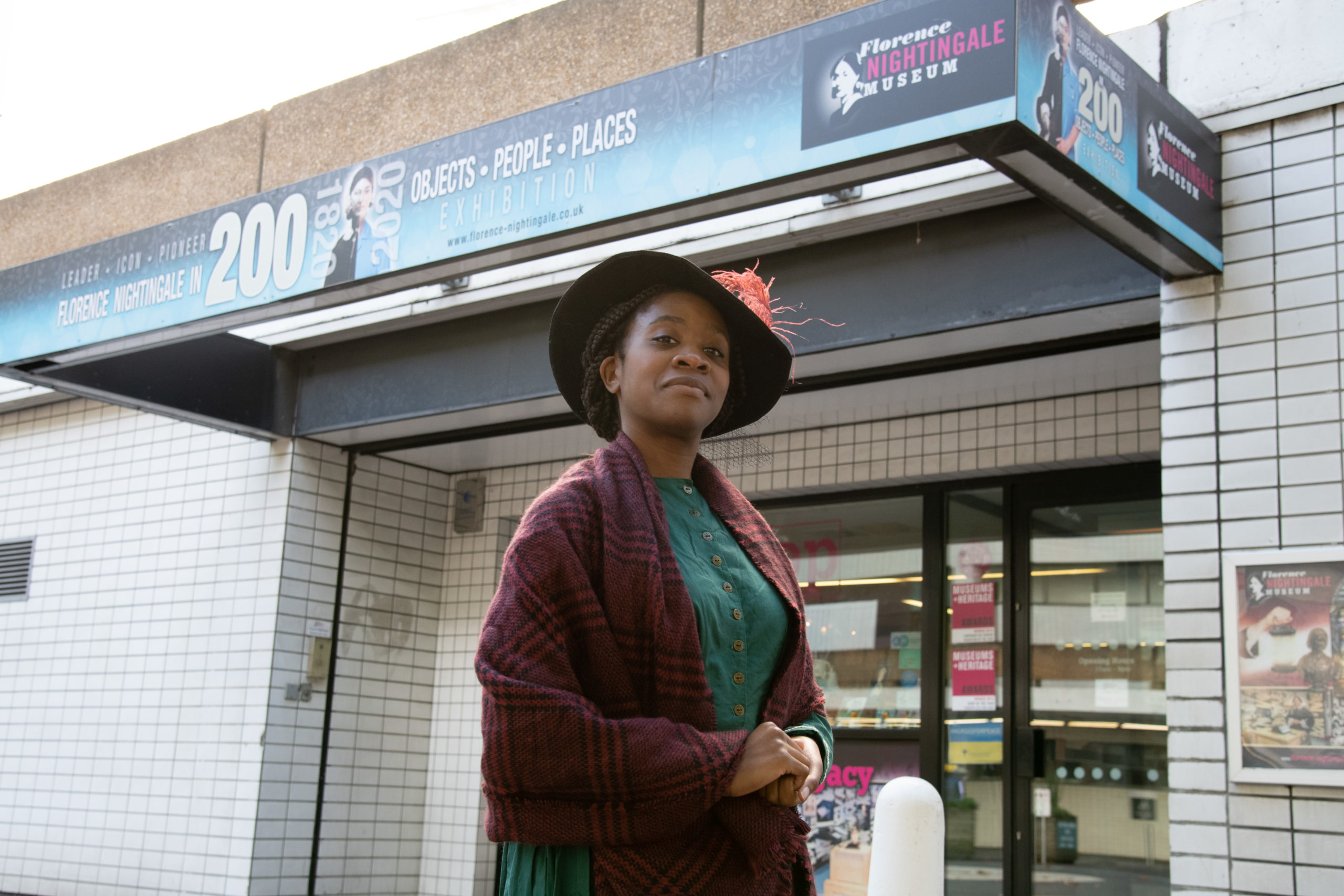 An actress is dressed in historical costume as Mary Seacole. She is standing outside the Florence Nightingale Museum.