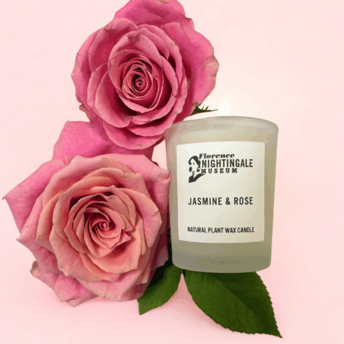 a votive candle with 2 large roses next to it on a pink background