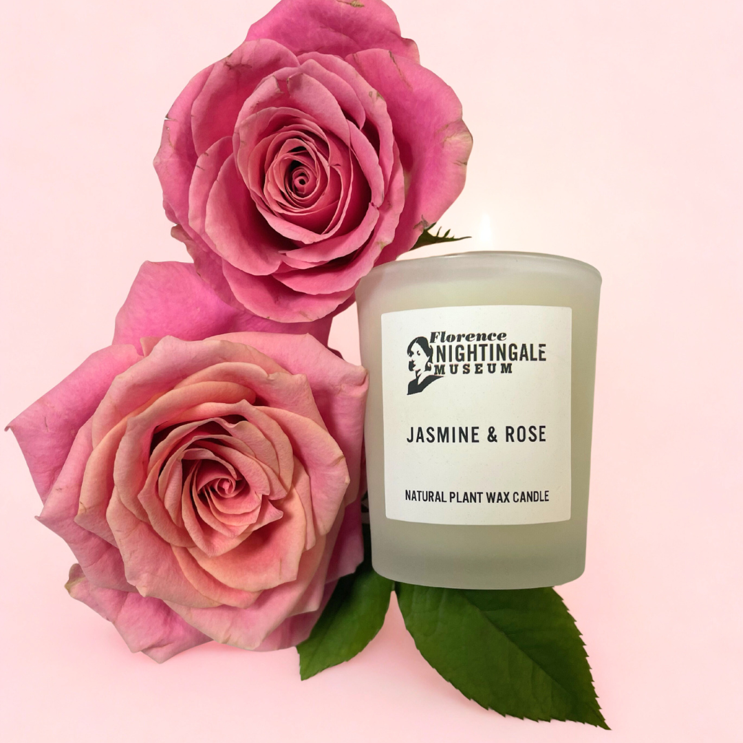 a votive candle with 2 large roses next to it on a pink background