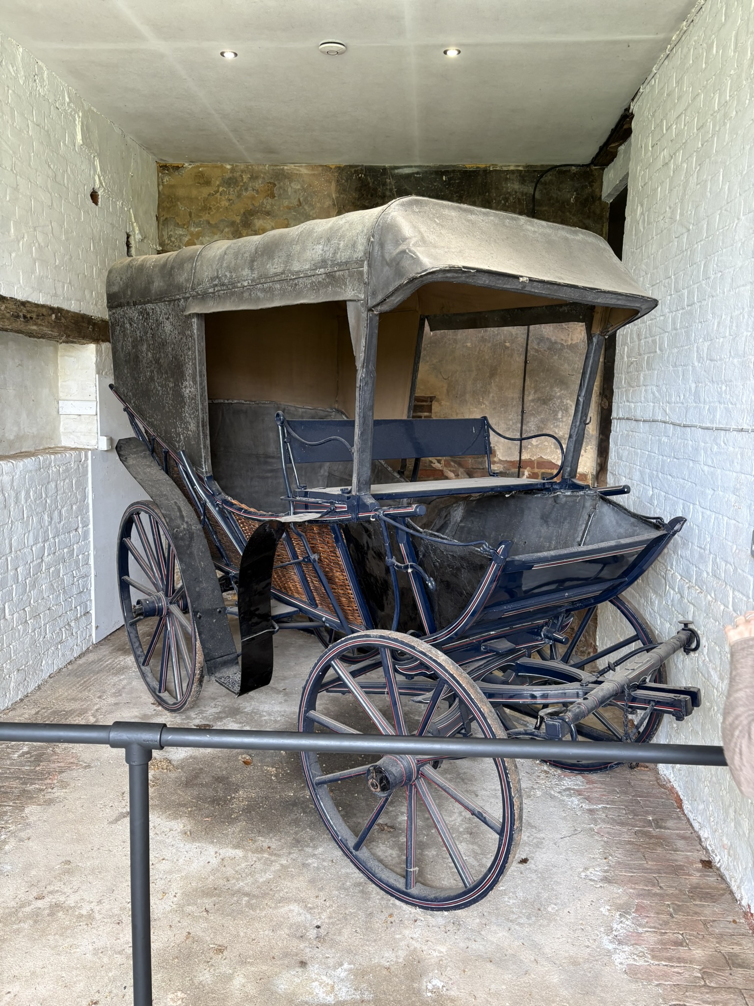 a colour photograph of a small carriage with a canopy in a white walled stable.