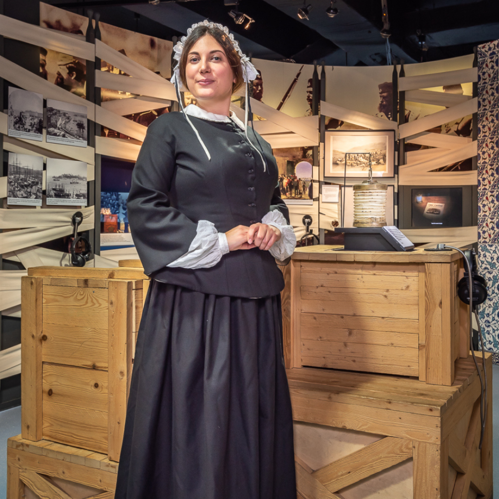 Florence Nightingale performer poses for a photo. She wears a black dress with a white collar, white undersleeves, and a white ruffled cap.